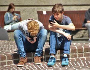 two teenagers sitting outside and staring at their phones